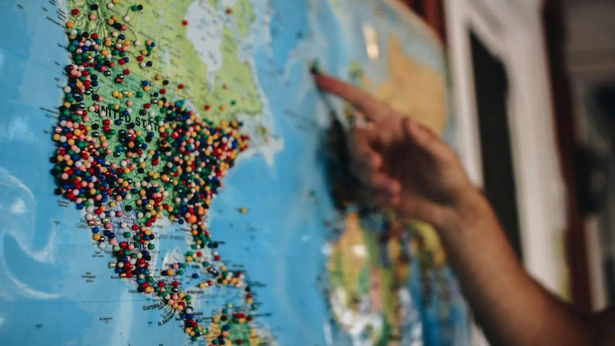 Main pointant une carte du monde colorée couverte d'épingles