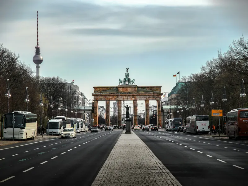 La porte de Brandebourg au bout d'une large avenue, avec la tour de télévision de Berlin en arrière-plan