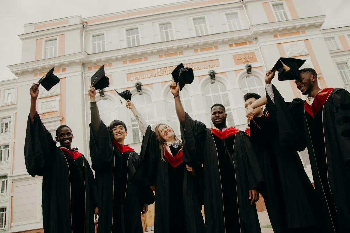 Des diplômés en toge noire lançant leur toque en l'air devant un bâtiment universitaire