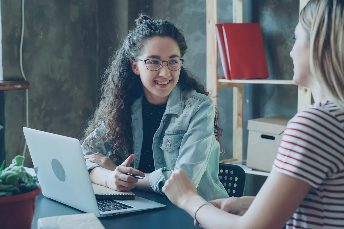 Jeune femme souriante échangeant avec un conseiller à un bureau, devant un ordinateur portable