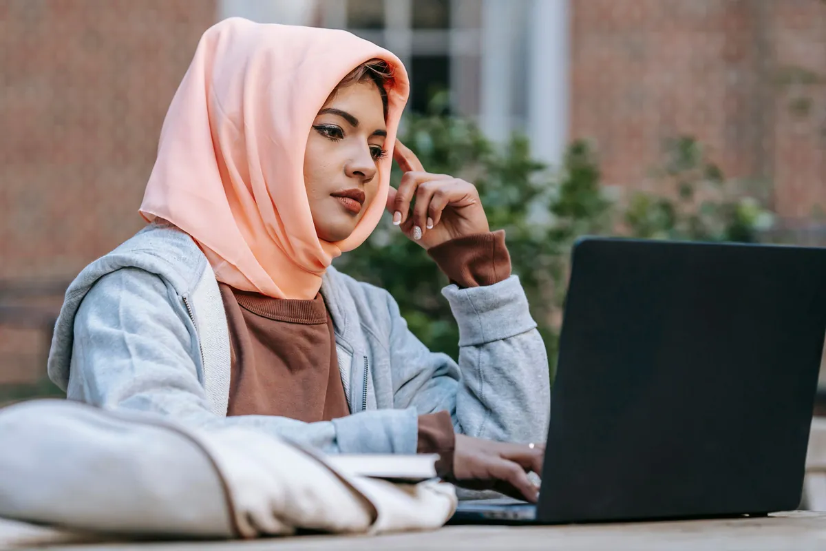 Jeune femme voilée étudiant sur son ordinateur portable en plein air